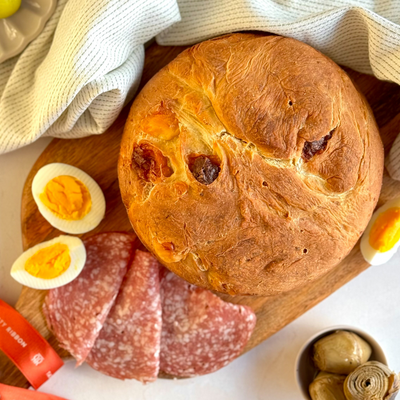 Italian Easter Cheese Bread on a wooden board, accompanied by cold cuts, veggies and boiled eggs.